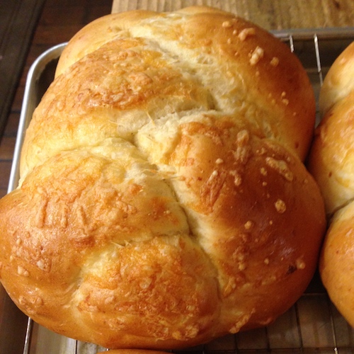 A round, golden Cheddar Cheese Bread on a wire cooling rack. Pulled-knot top, melted cheese baked into the crust.