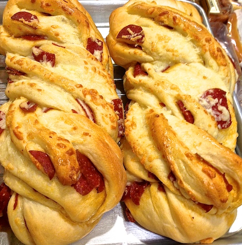 Two loaves of Pepperoni Cheese Twist Bread on a sheet pan. Pepperoni rounds tucked into braided dough, cheese melted between the folds.
