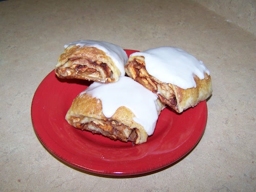 Three Wrapples on a red plate, vanilla icing still glossy on top, baked apples and piecrust folded together.